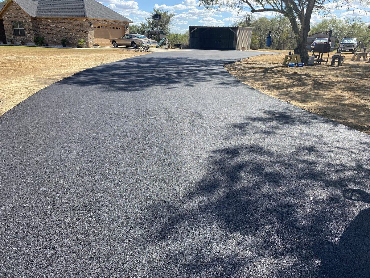 Freshly paved residential asphalt driveway leading to a stone home in the San Antonio area, completed by Lonestar Construction Industries